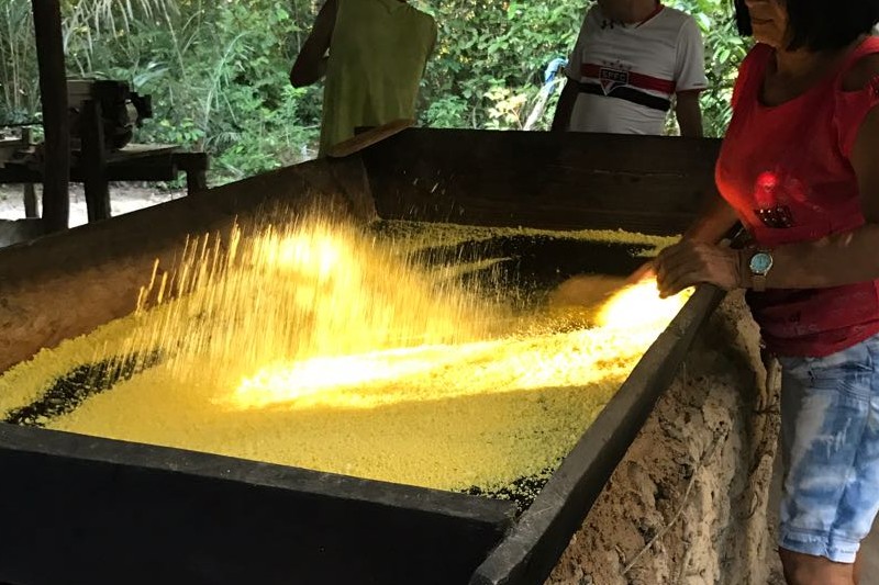 uma mulher fazendo farinha de mandioca no tacho