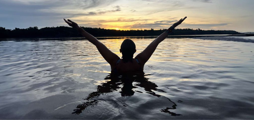 uma mulher mergulhando no rio negro ao pôr do sol